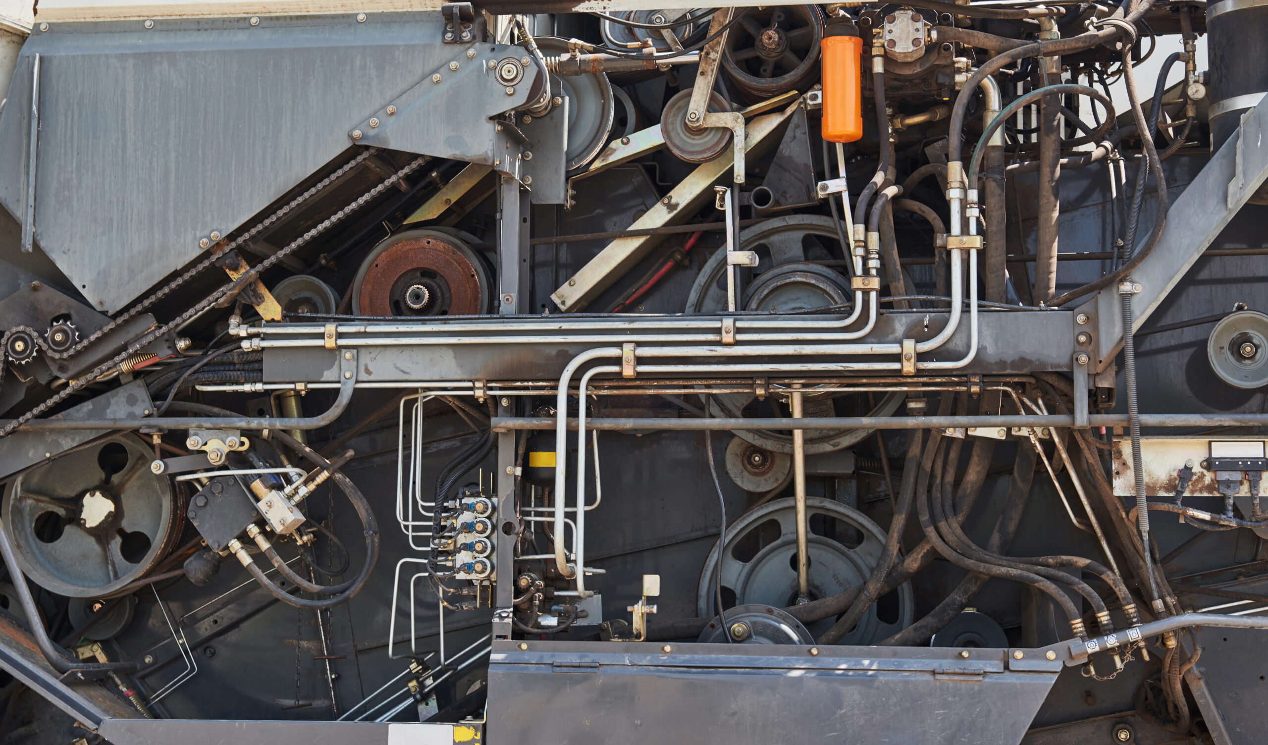 Detail vnitřních mechanických částí průmyslového stroje s hadicemi, řemenicemi a rozvody